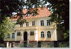 Ein Haus aus dem 19 Jhd., gelb angestrichen, umrahmt von B&auml;umen.